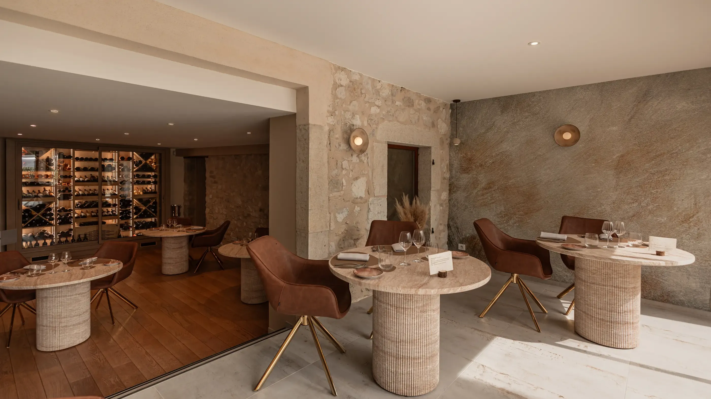 Salle de restaurant avec tables rondes en marbre, chaises en cuir brun et mur en pierre naturelle